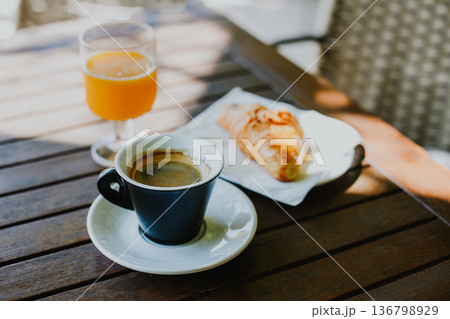 Cup of black coffee, a croissant and glass of fresh orange juice on a table in a street cafe. 136798929