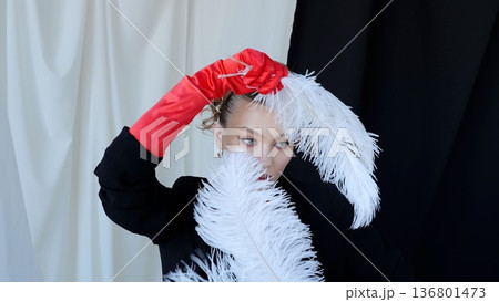 Stylish woman wearing red gloves is posing with white feathers in front of black and white background, creating an elegant and fashionable atmosphere 136801473