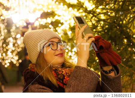 Delightful winter evening filled with lights as a woman captures the magic of twinkling decorations Delightful winter evening filled with lights as a woman captures the magic of twinkling decorations 136802011