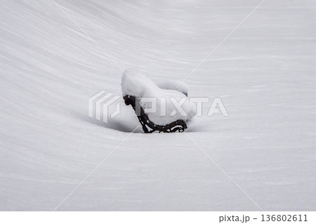 A bench covered in snow sits in the snow A bench covered in snow sits in the snow 136802611