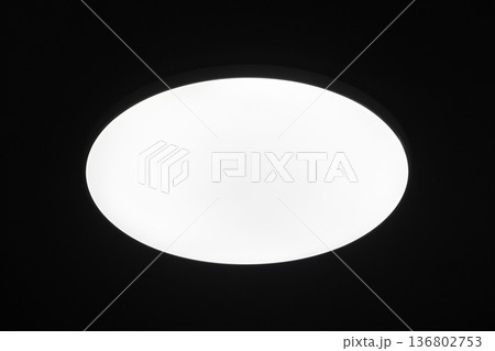 Bright circular ceiling light fixture casting an even white glow against a black ceiling Bright circular ceiling light fixture casting an even white glow against a black ceiling 136802753