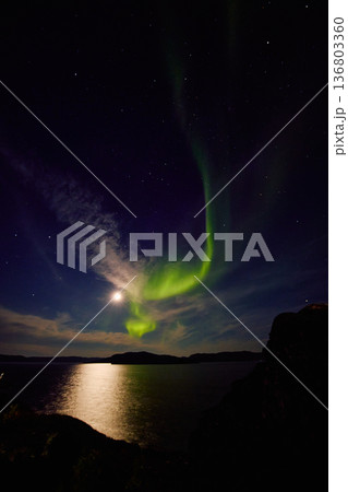 Aurora borealis over ocean in Teriberka, Russia, Murmansk region, Northern lights, Starry sky with polar lights and clouds. Night autumn landscape with bright aurora, stars, sea 136803360