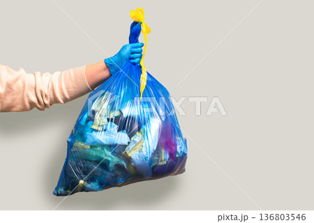 Hand holding full garbage bag on grey background isolated. High quality image 136803546