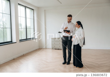 Notepad in hand, showing interior. Man and woman are in the modern new room, conception of business 136803672