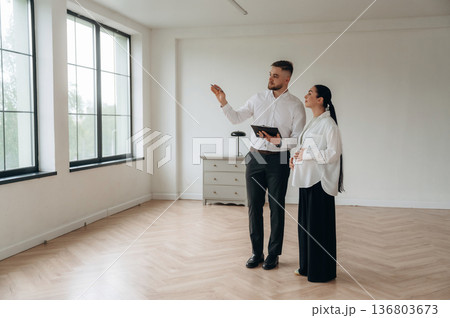 Notepad in hand, showing interior. Man and woman are in the modern new room, conception of business 136803673