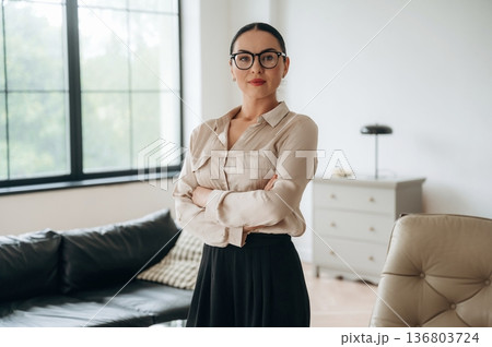 Arms crossed, standing. Woman in formal clothes is in the modern big room Arms crossed, standing. Woman in formal clothes is in the modern big room 136803724
