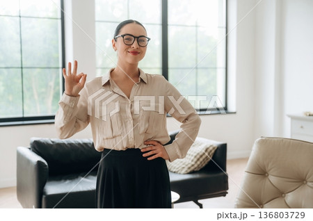 Okay hand sign. Woman in formal clothes is in the modern big room Okay hand sign. Woman in formal clothes is in the modern big room 136803729