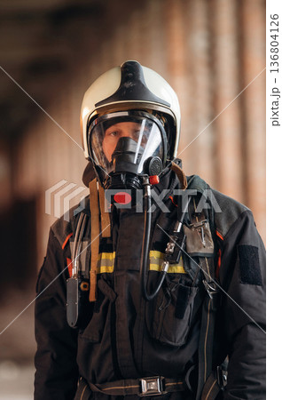 Protective air mask is on the face. Firefighter in professional equipment is indoors in abandoned building Protective air mask is on the face. Firefighter in professional equipment is indoors in abandoned building 136804126