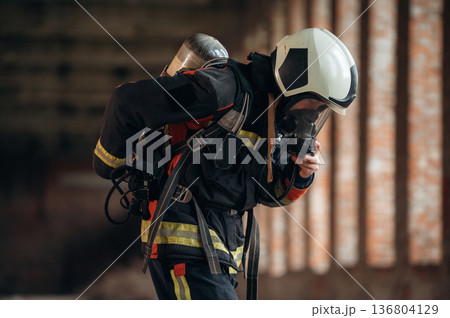 In mask, preparing air balloon. Firefighter in professional equipment is indoors in abandoned building 136804129