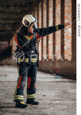 Standing in the abandoned building. Firefighter in professional equipment is indoors Standing in the abandoned building. Firefighter in professional equipment is indoors 136804138