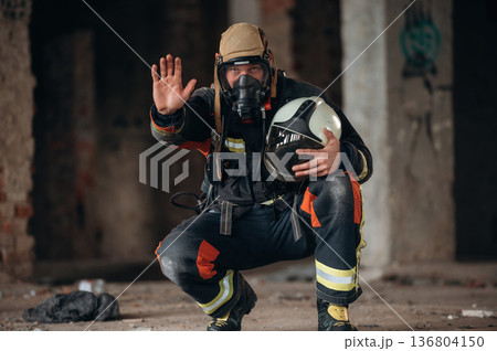 By the help of air mask. Firefighter in professional equipment is indoors in abandoned building 136804150