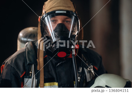 Front view, in the mask. Firefighter in professional equipment is indoors in abandoned building 136804151