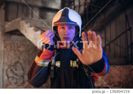 With walkie talkie radio. Firefighter in professional equipment is indoors in abandoned building With walkie talkie radio. Firefighter in professional equipment is indoors in abandoned building 136804159