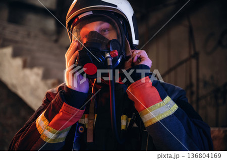 By the help of air mask. Firefighter in professional equipment is indoors in abandoned building 136804169
