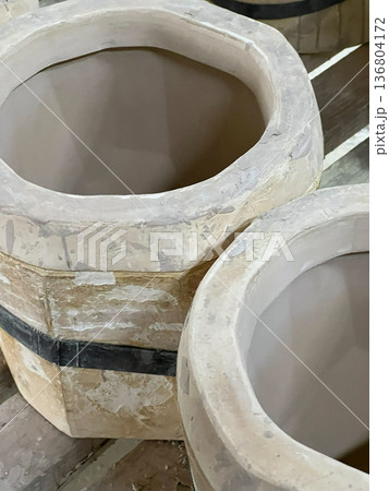 Two unglazed ceramic pots sit on a wooden shelf in a workshop, highlighting the clay shaping process Two unglazed ceramic pots sit on a wooden shelf in a workshop, highlighting the clay shaping process 136804172