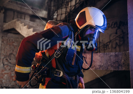 Adjusting air flow into the mask. Firefighter in professional equipment is indoors in abandoned building 136804199
