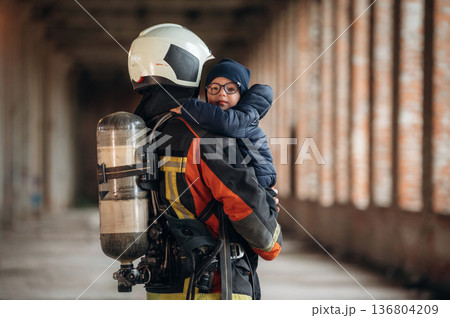 Holding kid in hands. Firefighter is with baby boy indoors Holding kid in hands. Firefighter is with baby boy indoors 136804209