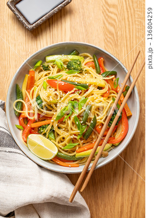 Stir fry wok noodles with vegetables in a plate on wooden countertop with chopsticks 136804259