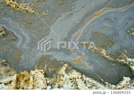 Iridescent oil slick spreading in a dirty asphalt puddle, causing environmental pollution and chemical waste 136804335