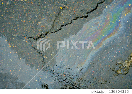 Iridescent oil slick on cracked wet asphalt surface showing rainbow colors and liquid texture. 136804336