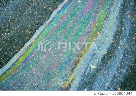 Oil spill on wet asphalt showing colorful iridescent gasoline film in sunlight. Concept of environmental pollution and danger 136804344