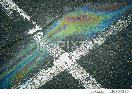 Oil spill creating rainbow sheen on wet asphalt road 136804359