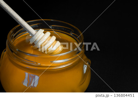 fresh honey is poured into a transparent jar on a black background 136804451
