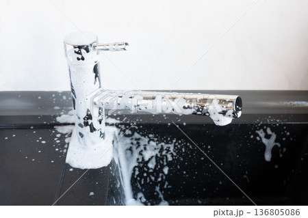 White foam for clean of water dripping of lime on metal tap. Cleaning of the house. Durty faucet in kitchen. White foam for clean of water dripping of lime on metal tap. Cleaning of the house. Durty faucet in kitchen. 136805086
