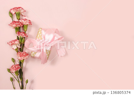 Carnations with a gift on a pink table, abstract spring floral background. Creative modern bouquet, minimal holiday concept. Greeting card for Women's Day or Mother's Day, 136805374