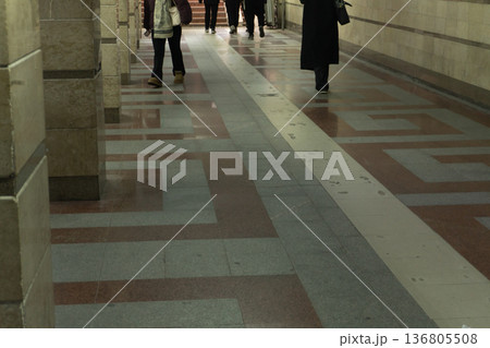 People walking in an underground subway station corridor. Perspective view of a tiled floor with geometric patterns. Urban public transport interior 136805508