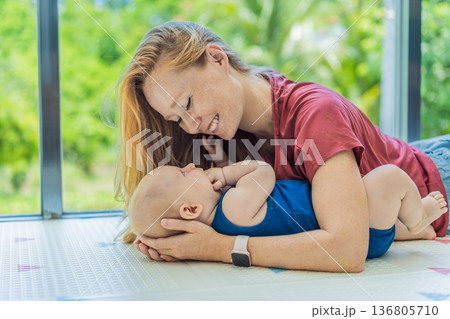 Mother and baby lying on a soft play mat at home, playing, talking and sharing a joyful moment together. Authentic family lifestyle, early childhood development and emotional bonding. Parenting and Mother and baby lying on a soft play mat at home, playing, talking and sharing a joyful moment together. Authentic family lifestyle, early childhood development and emotional bonding. Parenting and 136805710