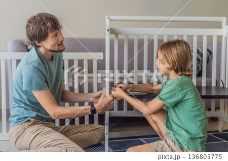 Father and older brother assembling a baby crib at home, preparing for a newborn arrival. Warm family moment full of care and anticipation. Parenthood, sibling bond and home preparation concept Father and older brother assembling a baby crib at home, preparing for a newborn arrival. Warm family moment full of care and anticipation. Parenthood, sibling bond and home preparation concept 136805775