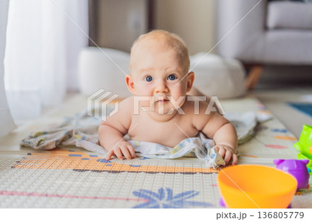Little baby playing with toys on a soft baby play mat at home. Early childhood development, sensory play, learning through play, curiosity, and happy infant activity concept for modern parenting. 136805779