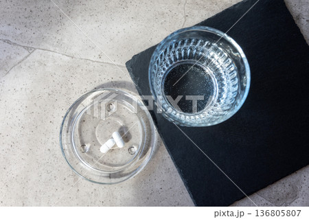 Pill and glass with water on the stone table. Healthcare from pharmacy. Person sit at home because of illness. Pill and glass with water on the stone table. Healthcare from pharmacy. Person sit at home because of illness. 136805807