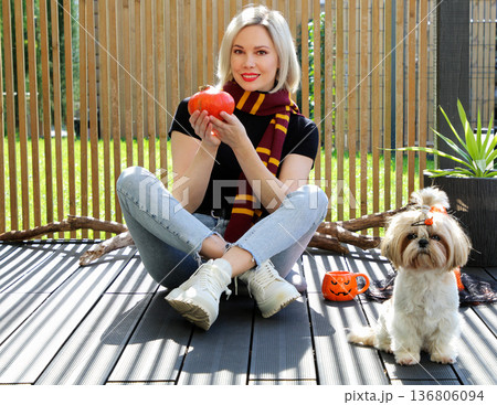 A beautiful girl is sitting on the terrace with a dog, holding a pumpkin in her hand. A beautiful girl is sitting on the terrace with a dog, holding a pumpkin in her hand. 136806094