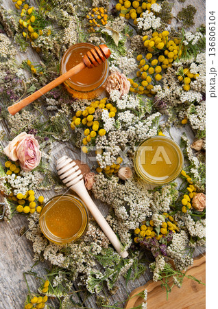 fresh natual different honey in glass jars with wooden honey spoons around herb flowers. flat lay fresh natual different honey in glass jars with wooden honey spoons around herb flowers. flat lay 136806104