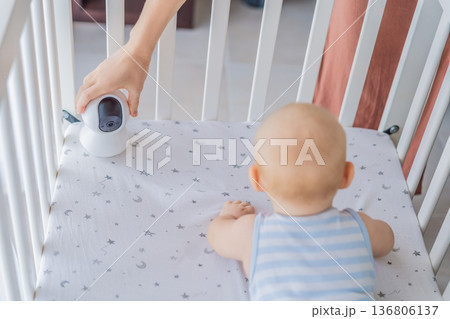 Baby monitor camera placed inside a crib where an infant is lying, ensuring safety and constant supervision. Modern parenting scene combining care and technology. Baby monitoring, security and smart 136806137