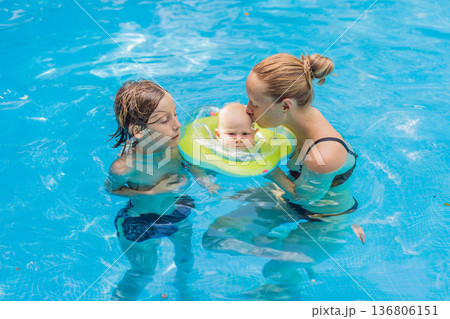 Mother with her older son and baby wearing a neck float enjoying time together in a swimming pool. Happy family water activity full of care and fun. Summer parenting, baby swimming and family bonding Mother with her older son and baby wearing a neck float enjoying time together in a swimming pool. Happy family water activity full of care and fun. Summer parenting, baby swimming and family bonding 136806151