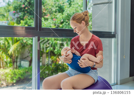 Young mother gently rocks her baby on a fitness ball at home, creating a calm loving atmosphere. Authentic family lifestyle, natural parenting and emotional bonding. Motherhood, wellbeing and baby Young mother gently rocks her baby on a fitness ball at home, creating a calm loving atmosphere. Authentic family lifestyle, natural parenting and emotional bonding. Motherhood, wellbeing and baby 136806155