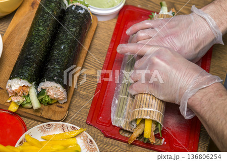 Process of making sushi and rolls. Close-up of man chef hands preparing traditional Japanese food at home or in restaurant on kitchen table. 136806254