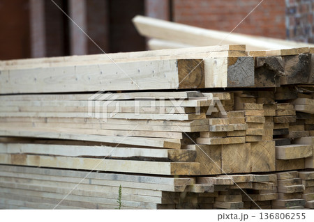 Stack of natural brown uneven rough wooden boards on building site. Industrial timber for carpentry, building, repairing and furniture, lumber material for roofing construction. 136806255