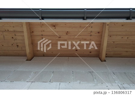 Building fasade under construction with unfinished wall and wooden roof boards with plastic gutter pipes. Building fasade under construction with unfinished wall and wooden roof boards with plastic gutter pipes. 136806317