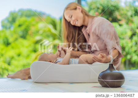 Newborn baby resting in a cozy cocoon beside mother with aroma lamp, calm home atmosphere. Infant relaxation, gentle care, motherhood routine, aromatherapy for babies and family wellbeing concept. 136806487