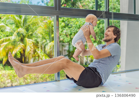 Father exercising with his small baby at home, active parenting and healthy lifestyle. Strong family bond, early physical development, modern fatherhood, fitness with children concept. 136806490