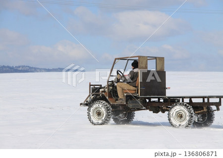 Rear side view of a man driving a homemade utility vehicle across a frozen, snow-covered field 136806871