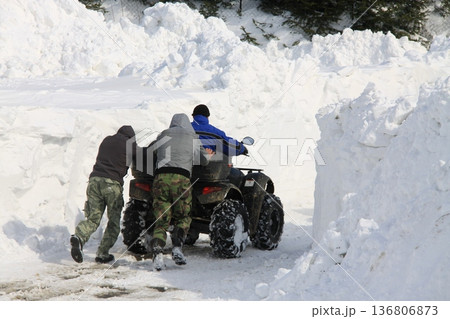 Three men push an ATV through a narrow path carved in deep snowbanks Three men push an ATV through a narrow path carved in deep snowbanks 136806873