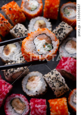 sushi roll in chopsticks beautiful served at black dish. top view. macro shot sushi roll in chopsticks beautiful served at black dish. top view. macro shot 136806887