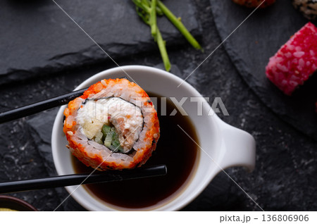sushi roll in chopsticks beautiful served at black dish. top view. macro shot sushi roll in chopsticks beautiful served at black dish. top view. macro shot 136806906