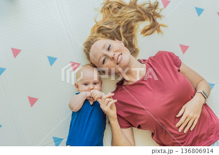 Mother and baby lying on a soft play mat at home, playing, talking and sharing a joyful moment together. Authentic family lifestyle, early childhood development and emotional bonding. Parenting and 136806914
