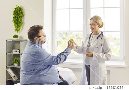 Nutritionist gives apple to patient while discussing healthy diet in clinic 136810354